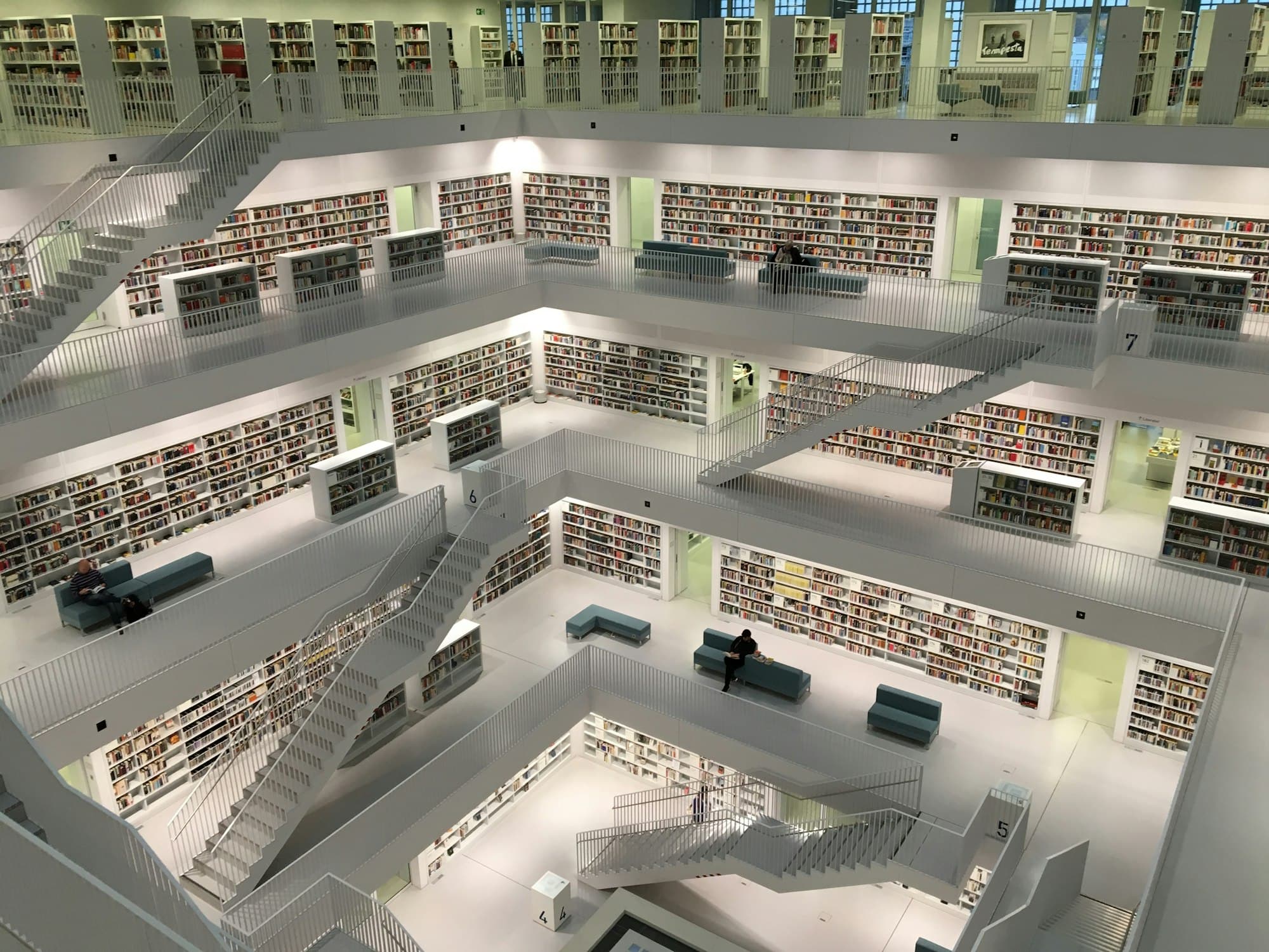 White multi-storey library with bookshelves, stairs and reading benches