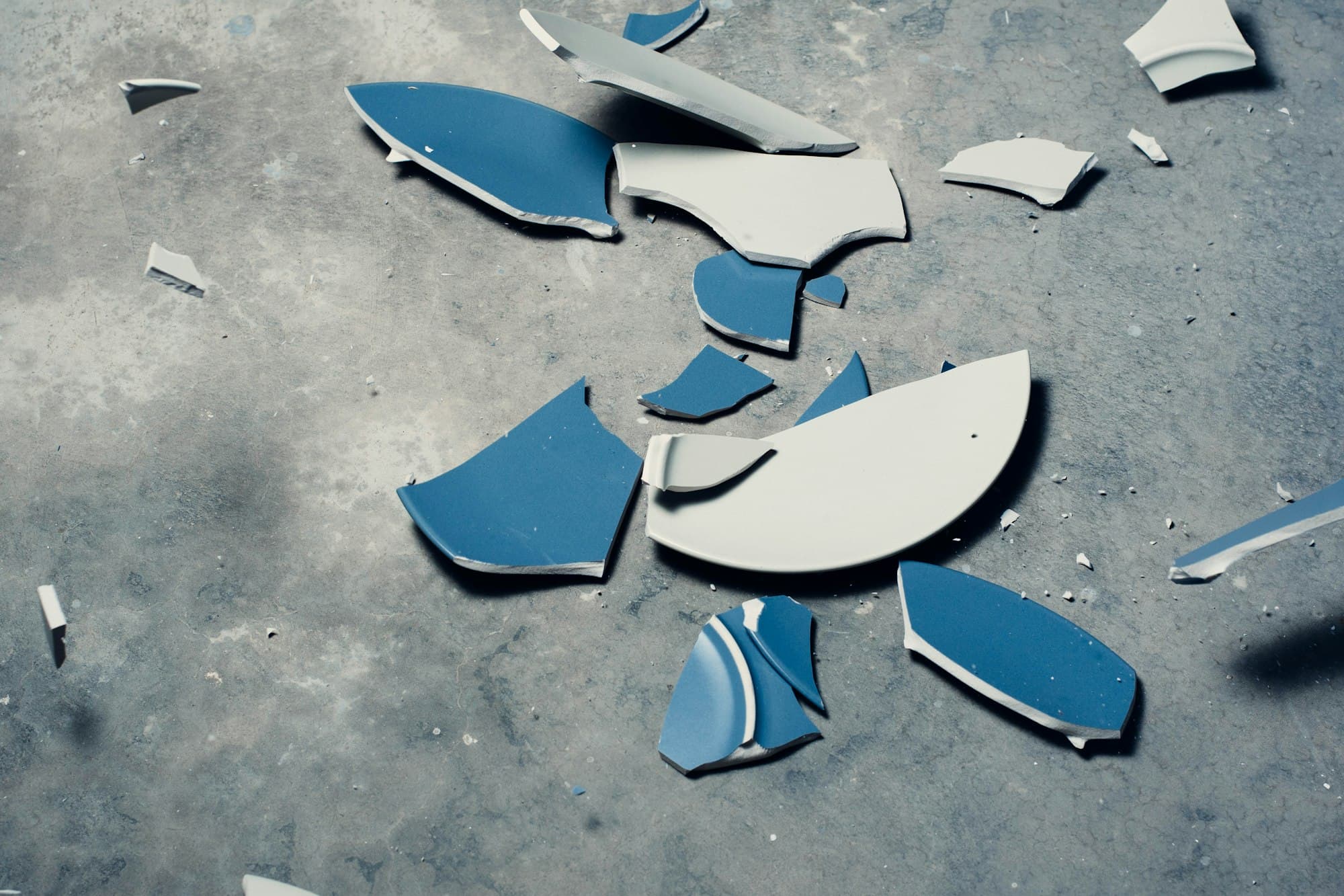 Broken blue and white plate pieces scattered on a grey surface