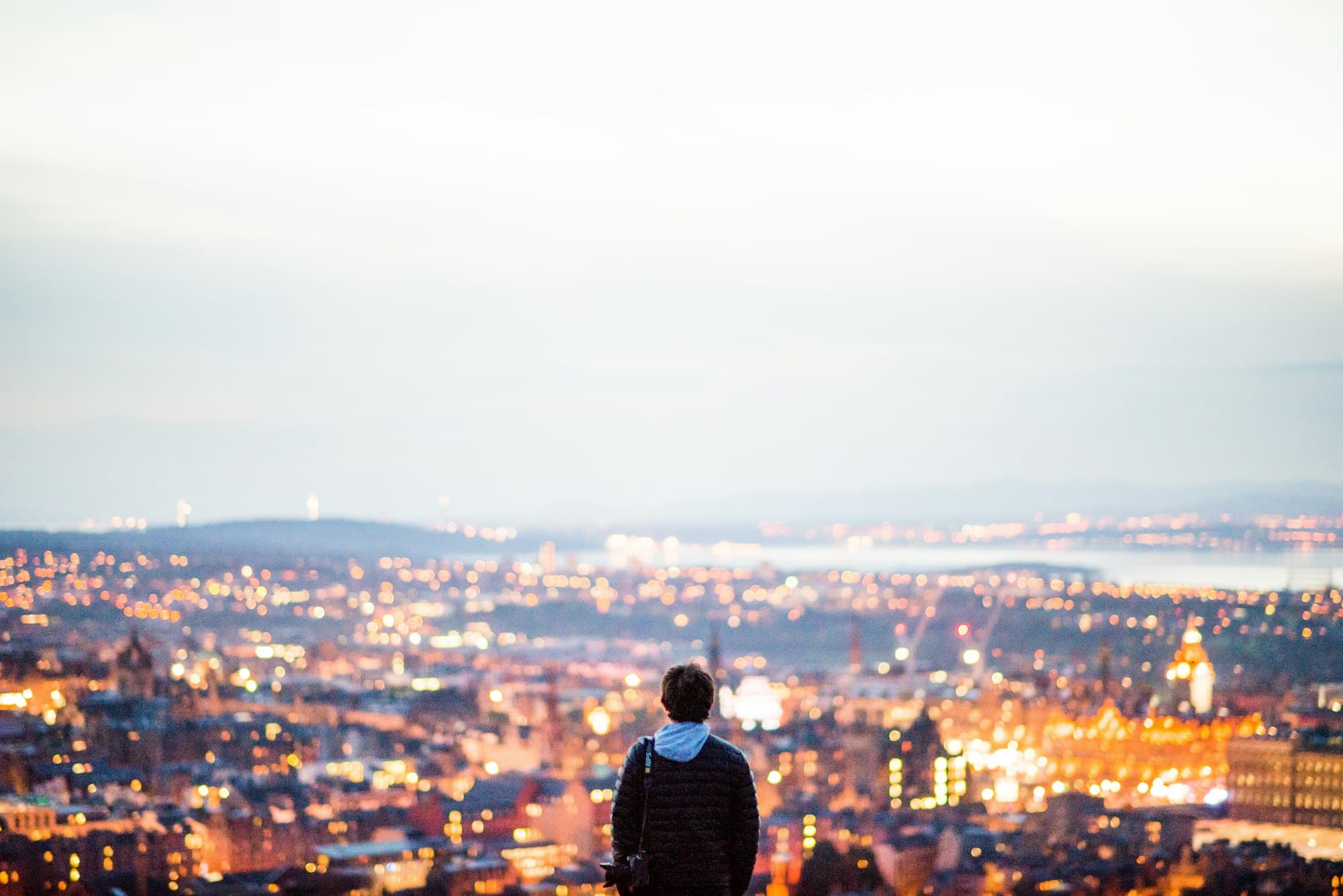 Person standing above a city at dusk, looking out over lights