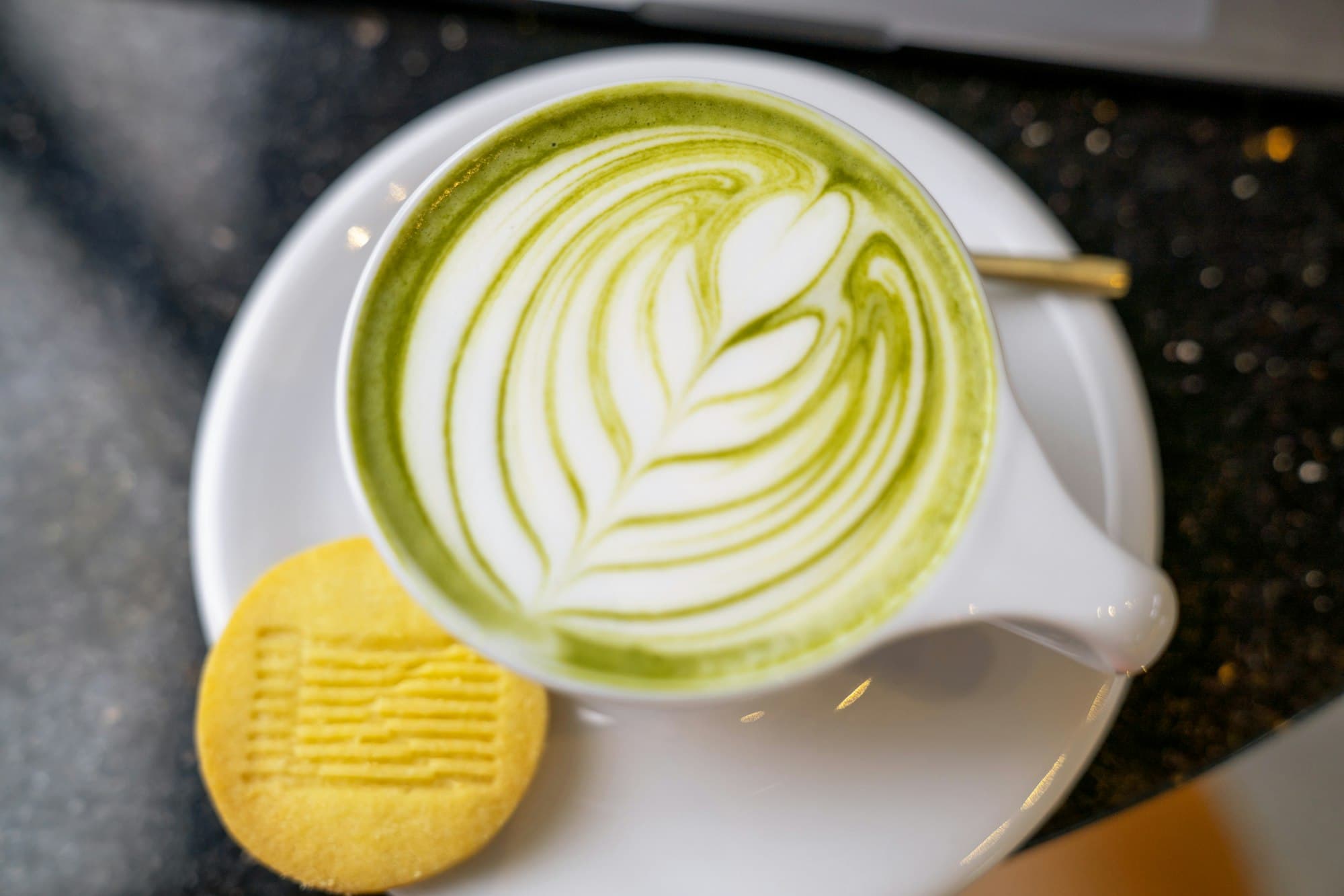 Matcha latte with leaf foam art and a shortbread biscuit on a saucer