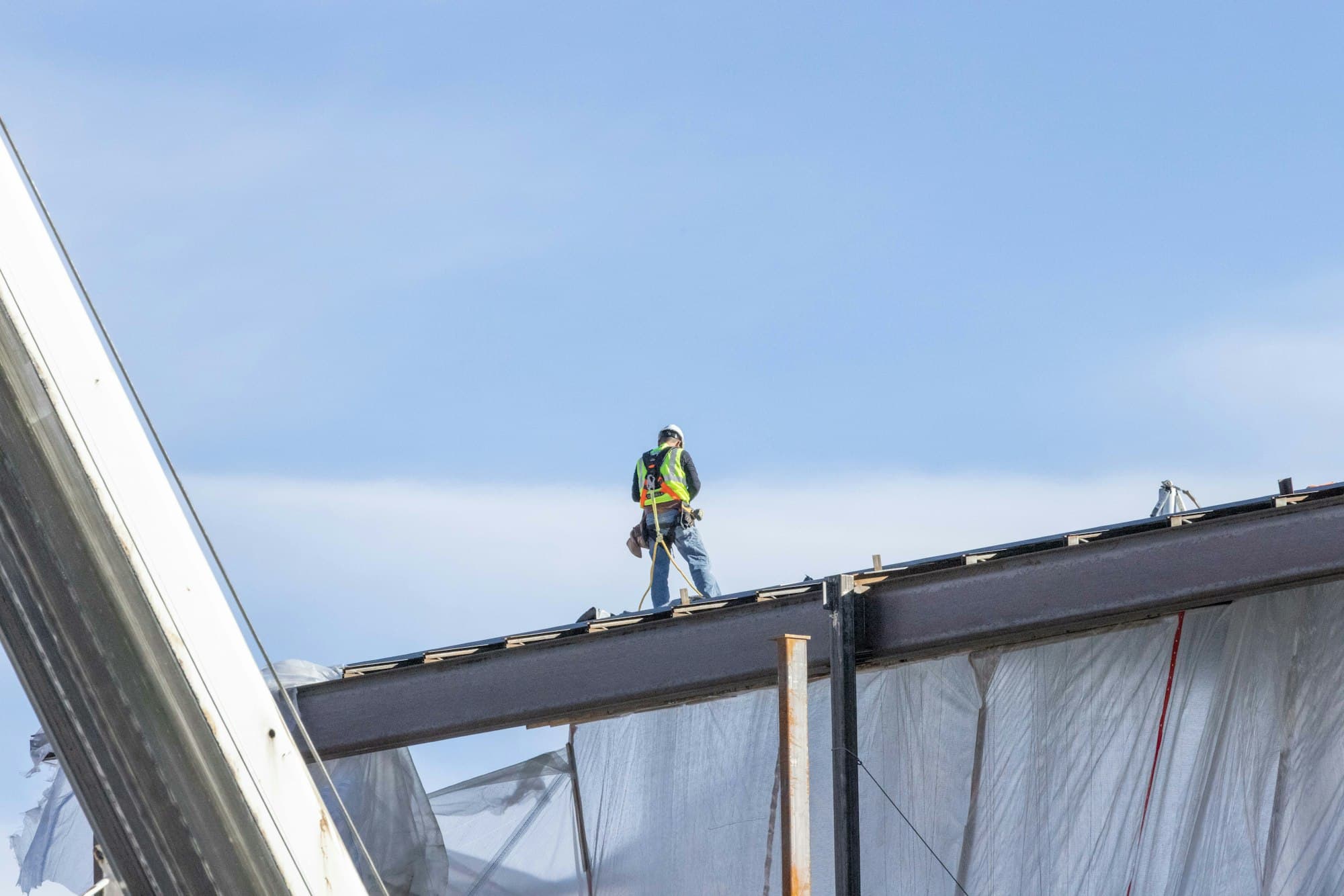 Construction worker in a hard hat standing on a steel beam against a blue sky